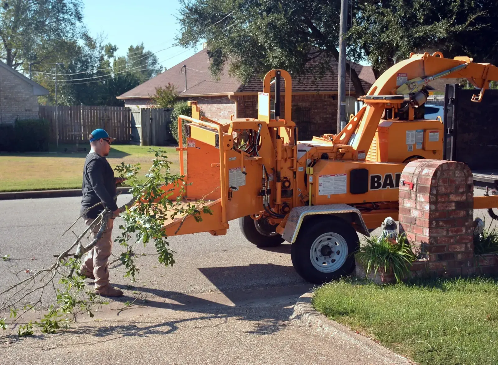 Tree service crew feeding cut branches into a wood chipper parked on a residential driveway